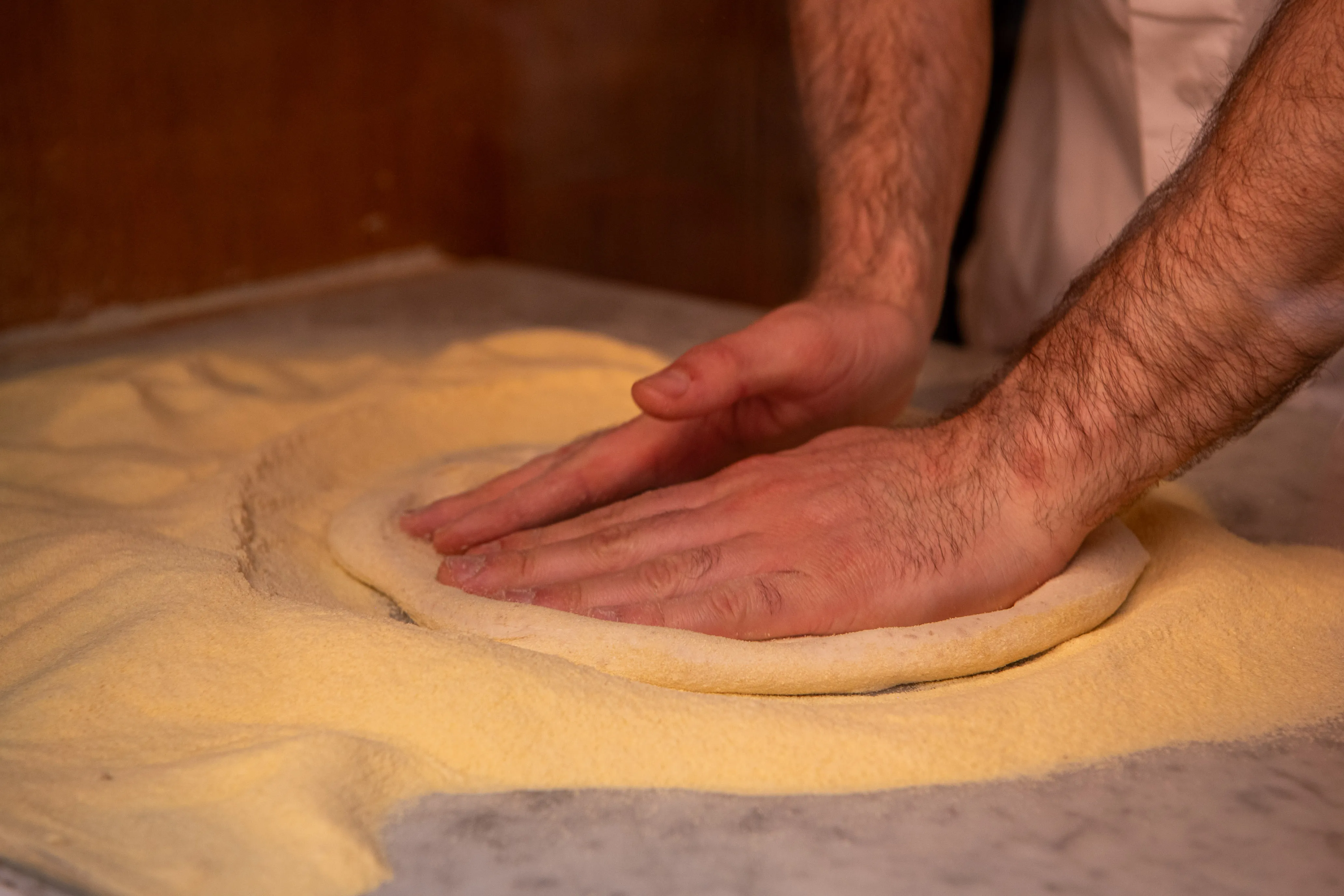 Mani del pizzaiolo che lavorano l'impasto per la pizza con lievito madre